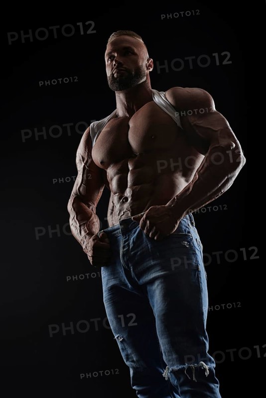 Muscular model man in white t-shirt on a black background. Sporty guy showing his big shoulders