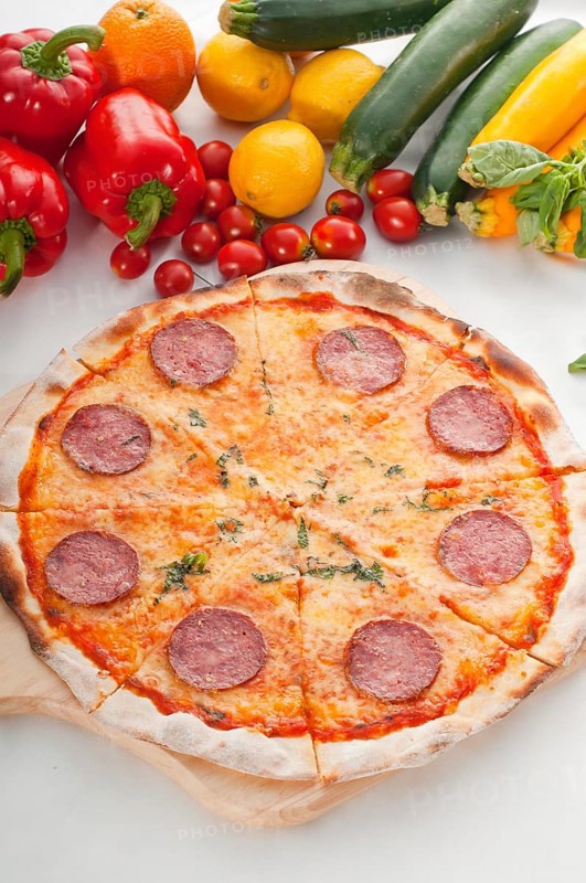 Italian original thin crust pepperoni pizza with fresh vegetables on background