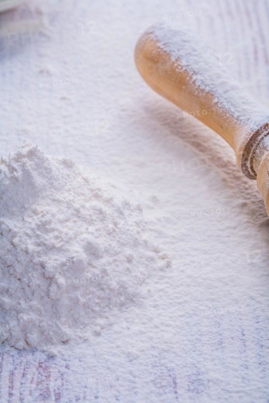 Small pile of white natural flour and wooden rolling pin in vertical version