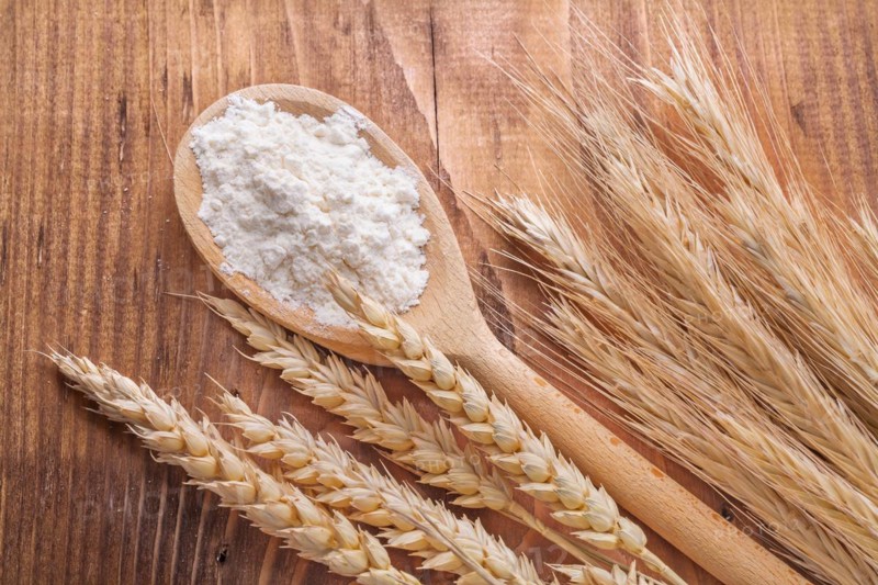 Flour in wooden spoon and wheat ears on vintage board food and drink concept