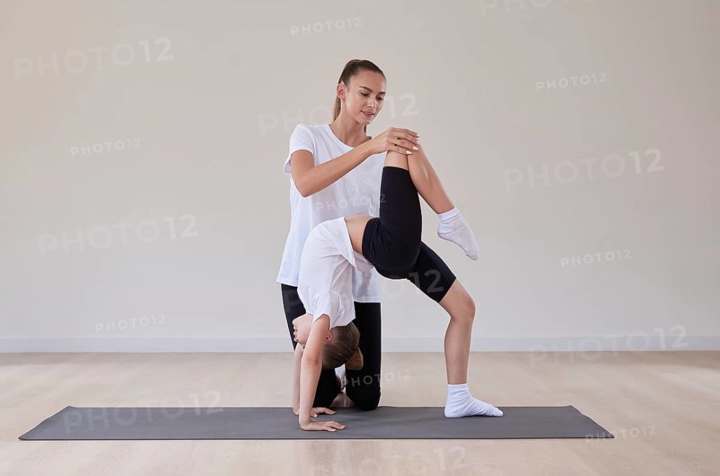 Beautiful female teacher helps a little girl stretch in a gymnastics class. The concept of education