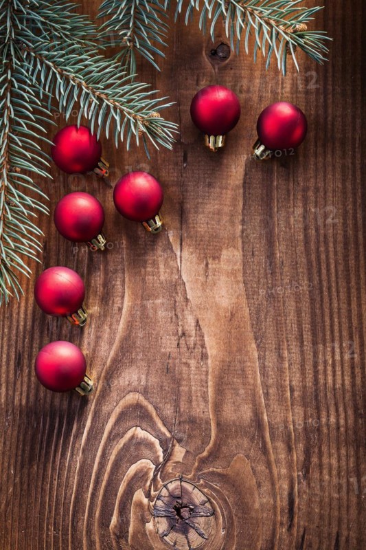 Small red Christmas baubles with fir tree branches on an old wooden board with copy space
