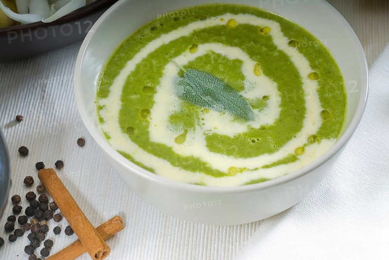 Fresh spinach soup on a white bowl with sage and cream on top