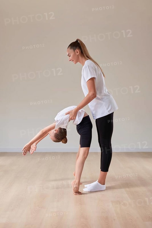 Beautiful female teacher helps a little girl stretch in a gymnastics class. The concept of education