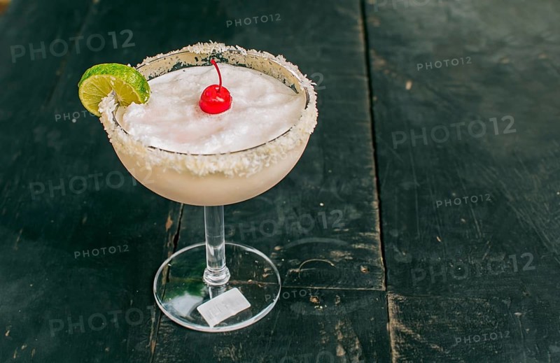 Frozen coconut margarita with lemon slice served on wooden table. Close up of delicious frozen coconut cocktail with cherry