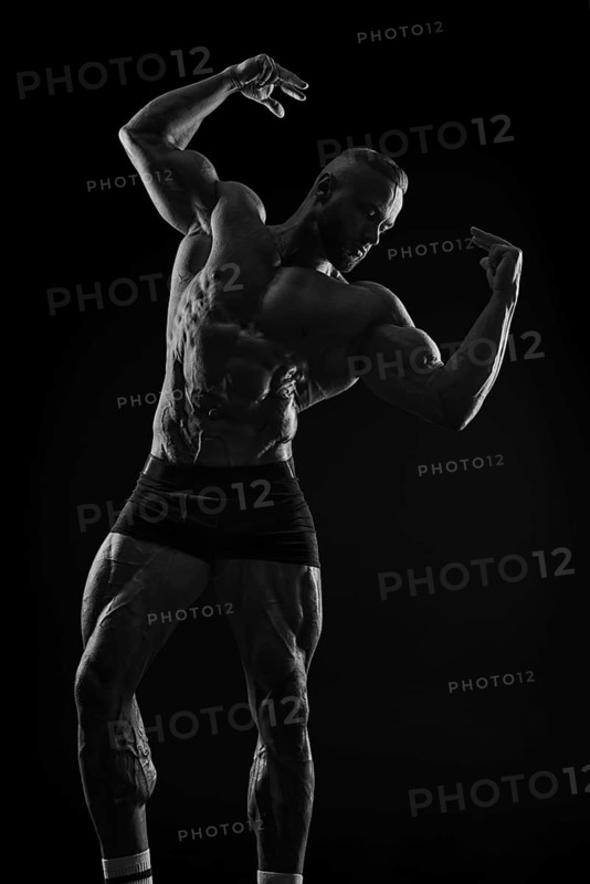 Silhouette of a strong bodybuilder. Confident young fitness athlete with a powerful body and perfect abs. Black and white photography. Dramatic light. Mixed media