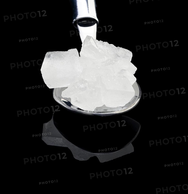 Crystal sugar on a spoon over black reflective surface background