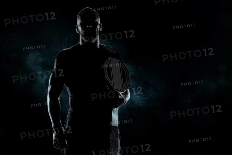 Kickboxer with a belt on his shoulder poses against a background of smoke. Sports competitions. Fight night. The concept of mixed martial arts. MMA