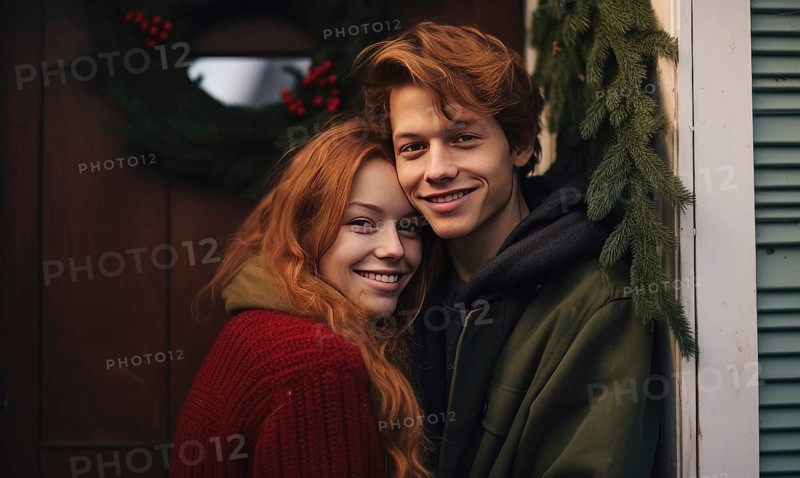 Young couple smiling together near home door decorated with mistletoe. Christmas holidays