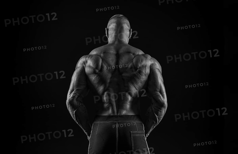 Silhouette of a strong bodybuilder. View from the back. Confident young fitness athlete with a powerful body and perfect abs. Black and white photography. Dramatic light