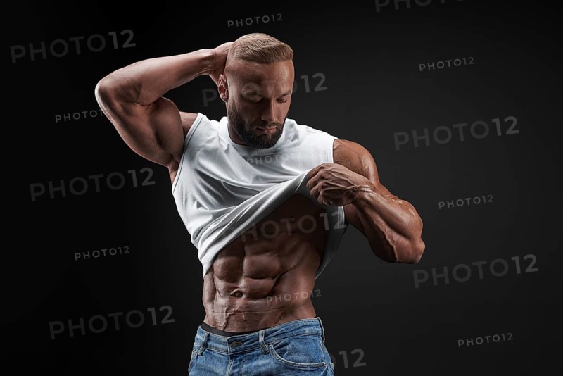 Muscular model man in white t-shirt on a black background. Sporty guy showing his big shoulders
