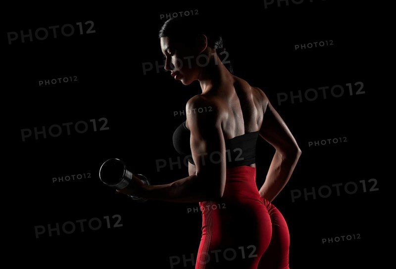 Brutal sports woman pumps up muscles with dumbbells. Fitness concept. Mixed media