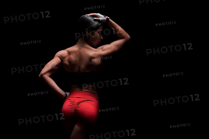 Athletic young woman showing back and arm muscles on isolated black background. Mixed media
