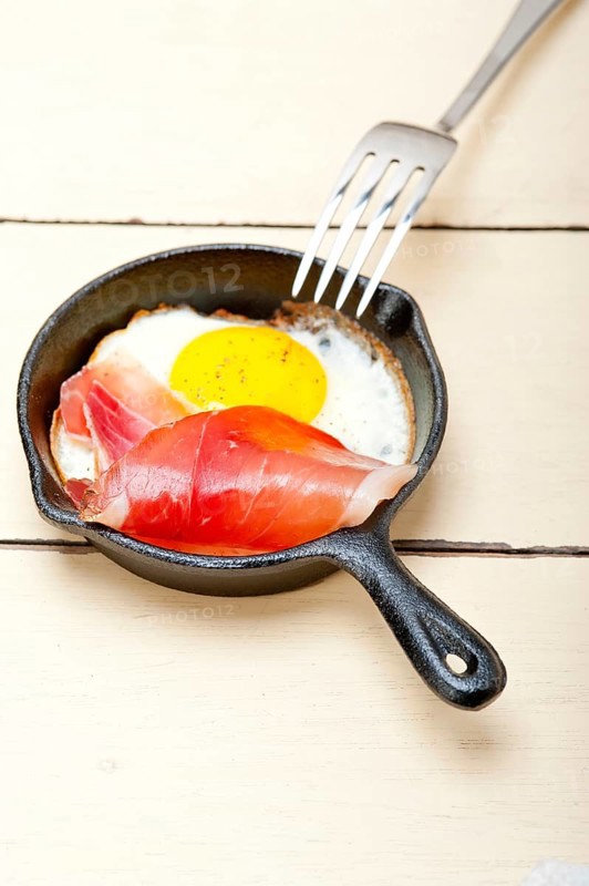 Fried egg sunny side up with Italian tyrolean speck smoked ham on a skillet
