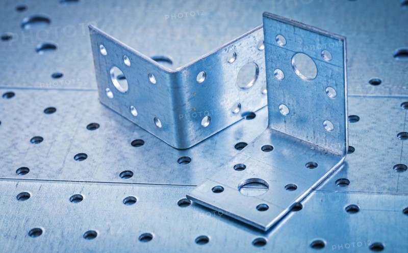 Stainless drilled angle iron on perforated metallic background Construction concept