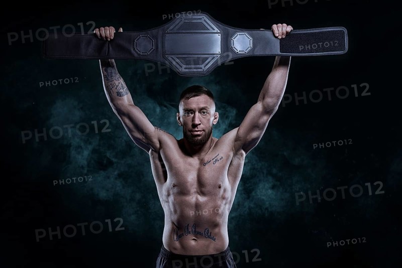 Kickboxer victoriously raises the belt won in the tournament against the backdrop of smoke. Sports competitions. Fight night. The concept of mixed martial arts. MMA