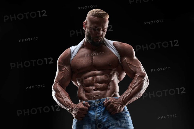 Muscular model man in white t-shirt on a black background. Sporty guy showing his big shoulders