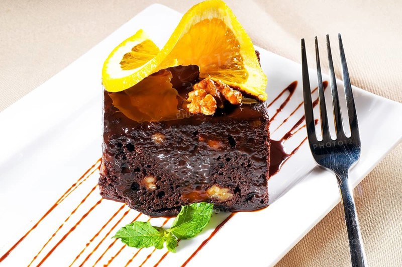 Fresh baked delicious chocolate and walnuts cake with slice of orance on top and mint leaf