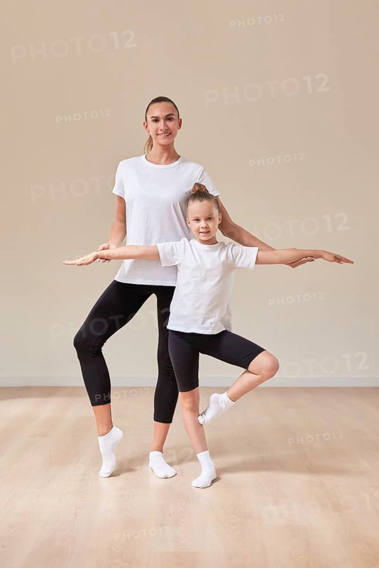 Beautiful woman teacher and a little girl perform dance movements in a bright studio. The concept of education