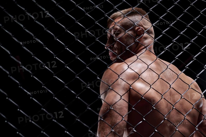 Dramatic image of a mixed martial arts fighter standing in an octagon cage. The concept of sports