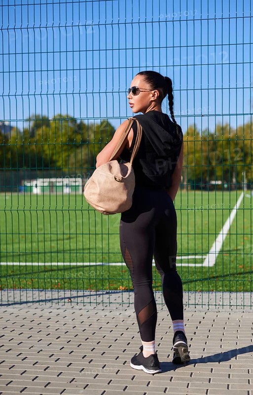 Pretty young fitness girl getting ready for a workout at the stadium. Attractive slim brunette in a tracksuit with a sports bag goes to the locker room. Active lifestyle