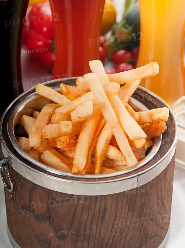 Fresh french fries on a wood bucket with selection of beers and fresh vegetables on background
