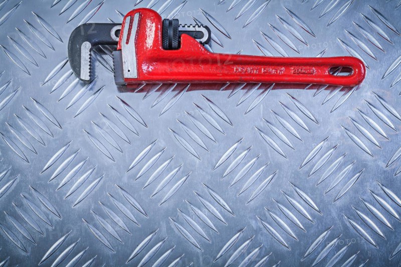 Adjustable monkey spanner on channeled metal background construction concept