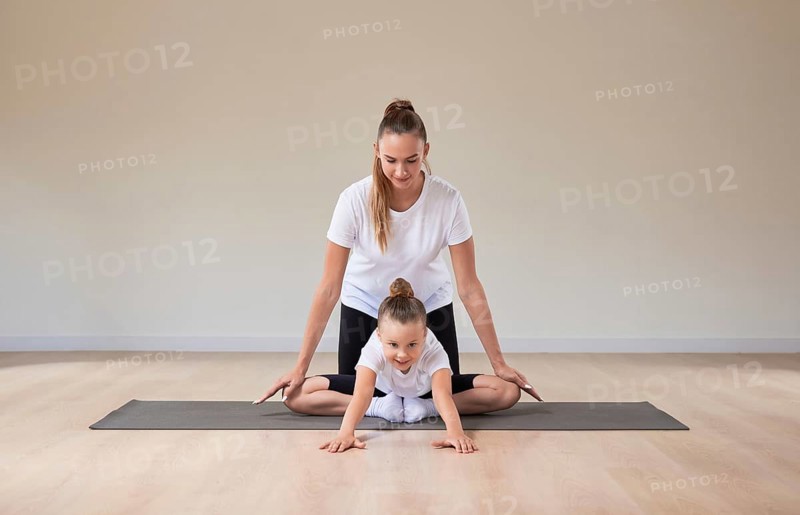 Beautiful female teacher helps a little girl stretch in a gymnastics class. The concept of education