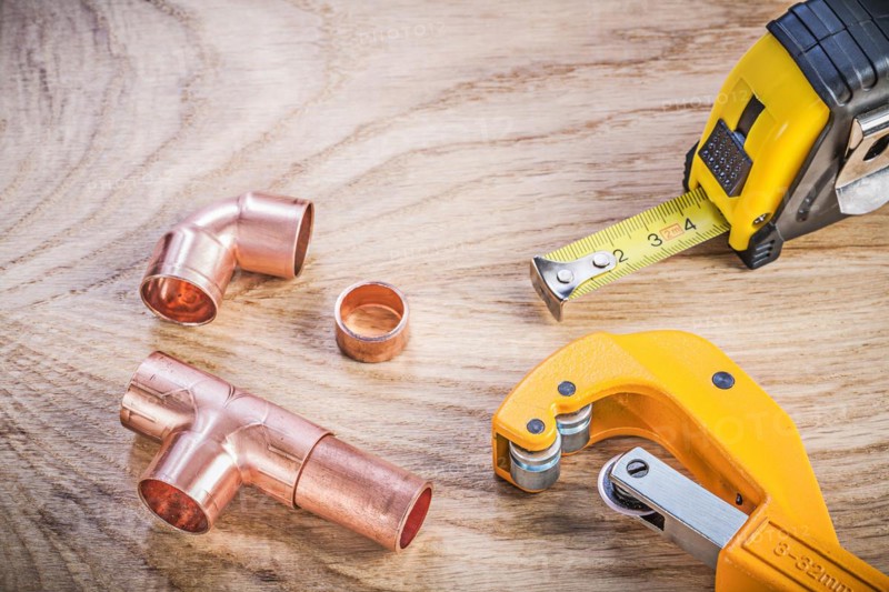 Composition of brass pipe cutter fittings measuring tape on wooden board plumbing concept