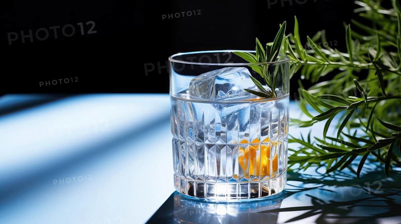 A glass of water with reflections and light refractions next to a plant
