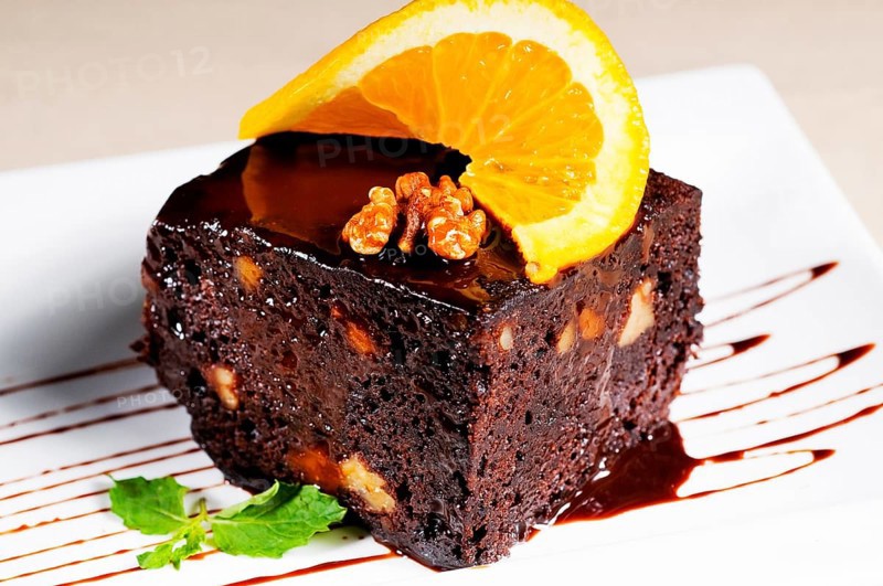 Fresh baked delicious chocolate and walnuts cake with slice of orance on top and mint leaf