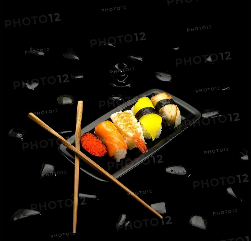 Assorted sushi plate on black pebbles over black background