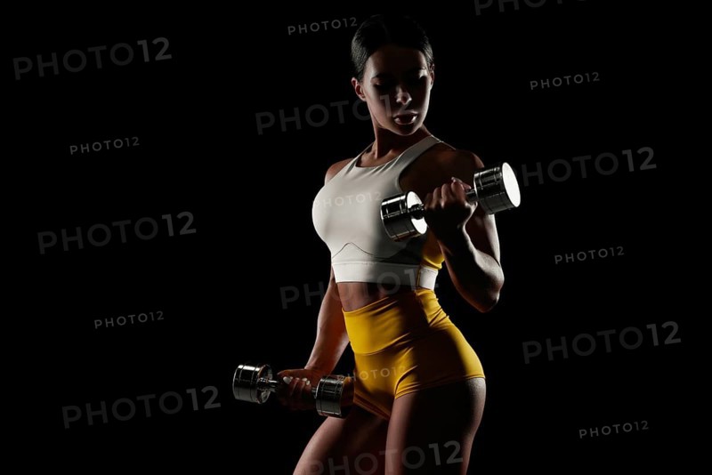 Brutal sports woman pumps up muscles with dumbbells. Fitness concept. Mixed media