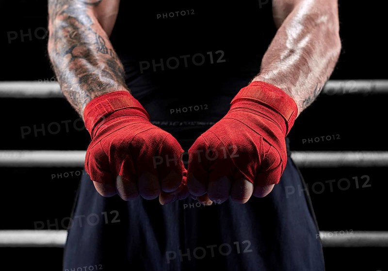 Red bandages on the hands of a kickboxer against the background of the ropes of the ring. The concept of mixed martial arts. MMA
