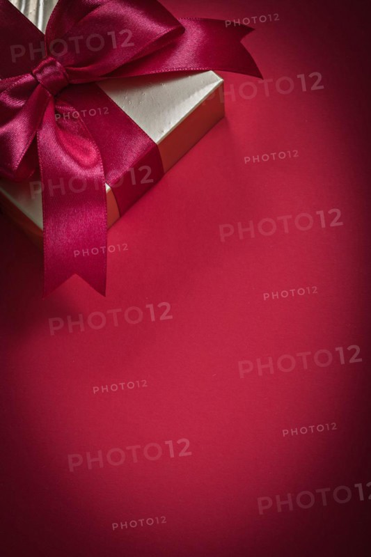 Wrapped giftbox with tied bow on red background holidays concept