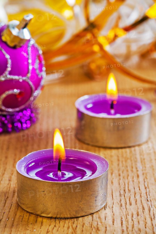 Two small glowing candles and Christmas baubles on a wooden board