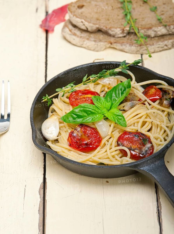 Italian spaghetti pasta with baked tomatoes basil and thyme sauce on a cast iron skillet