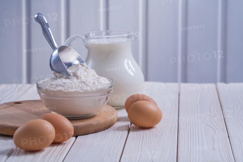 Composition bowl with flour scop eggs milk in pitcher on white painted old wooden board food and drink concept