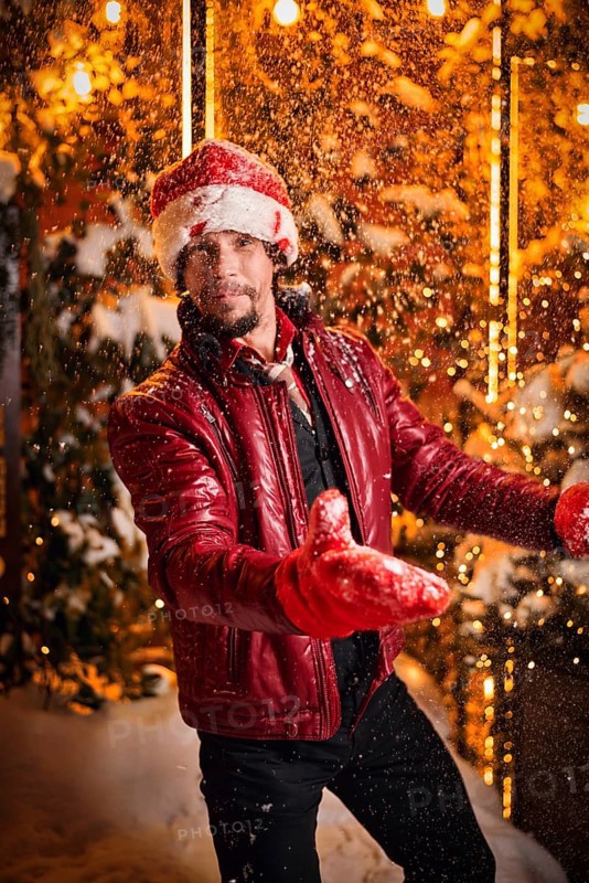 Man dressed as Santa Claus throws up snow on a street decorated with garlands. New Year and Christmas concept. Mixed media