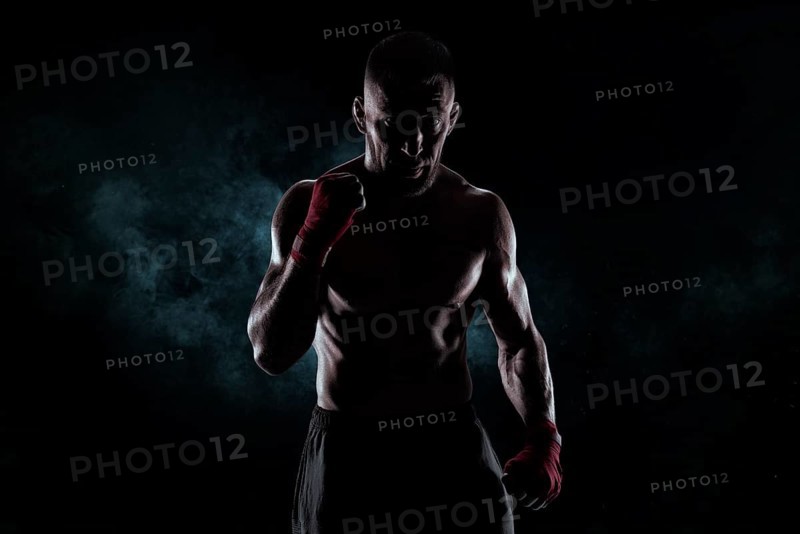 Kickboxer in red bandages poses against a background of smoke. The concept of mixed martial arts. MMA