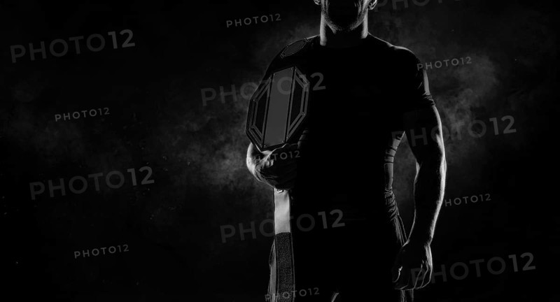 Kickboxer with a belt on his shoulder poses against a background of smoke. Sports competitions. Fight night. The concept of mixed martial arts. MMA