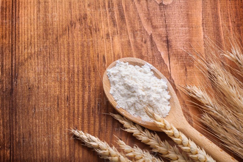Flour in wooden spoon with ears of wheat on wooden table with copy space