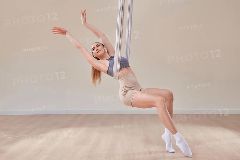 Image of a beautiful woman posing in a bright studio near the hammocks. The concept of airstretching. Fitness and sports