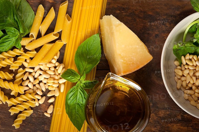 Italian basil pesto ingredients and raw pasta over old wood macro