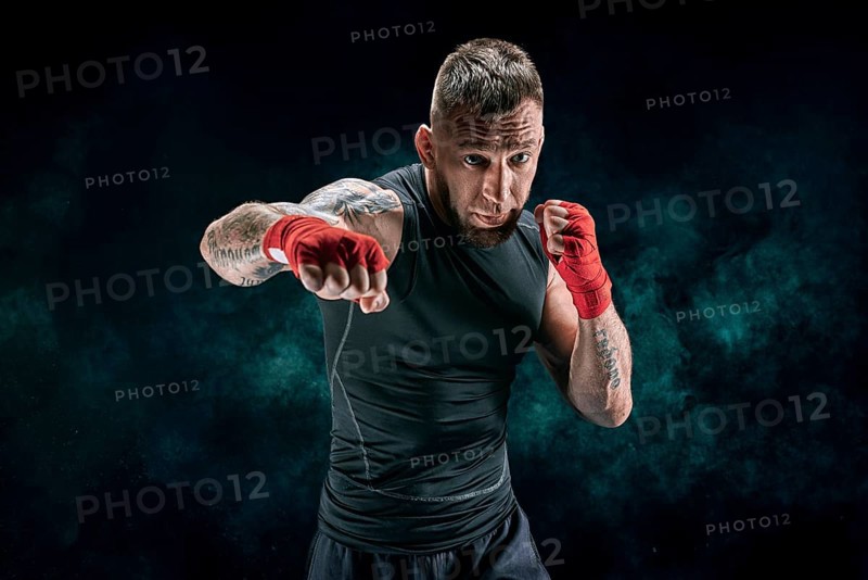 Kickboxer in red bandages is boxing against a background of smoke. The concept of mixed martial arts. MMA