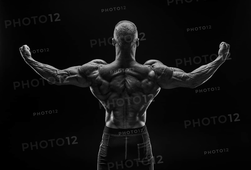 Silhouette of a strong bodybuilder. View from the back. Confident young fitness athlete with a powerful body and perfect abs. Black and white photography. Dramatic light