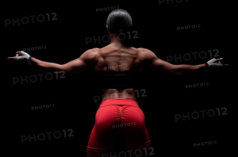 Athletic young woman showing back and arm muscles on isolated black background. Mixed media