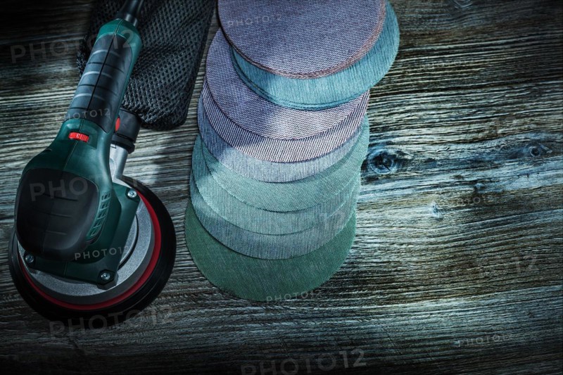 Electric orbit wood sander with sanding discs on dark vintage wooden background