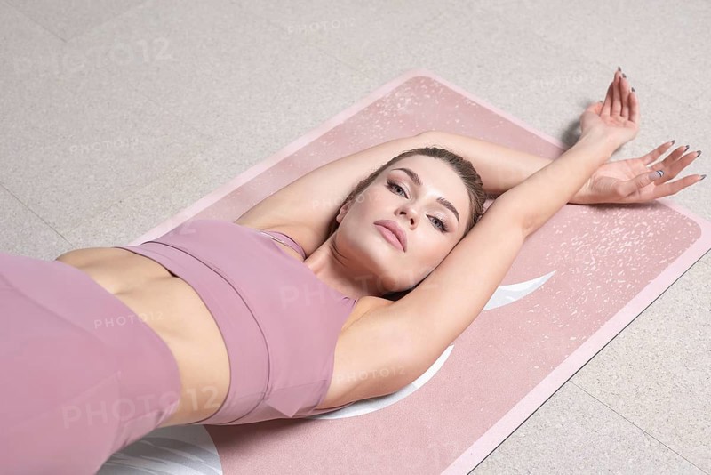 Beauty portrait of a charming woman in a gymnastic suit lying on a mat in a bright studio. The concept of fitness
