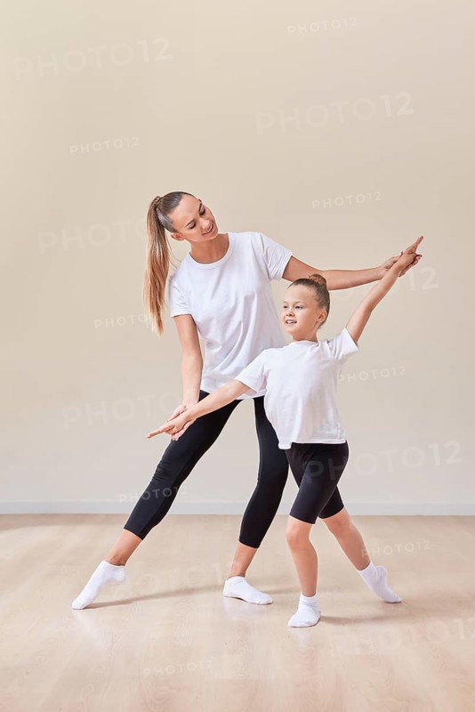 Beautiful woman teacher and a little girl perform dance movements in a bright studio. The concept of education